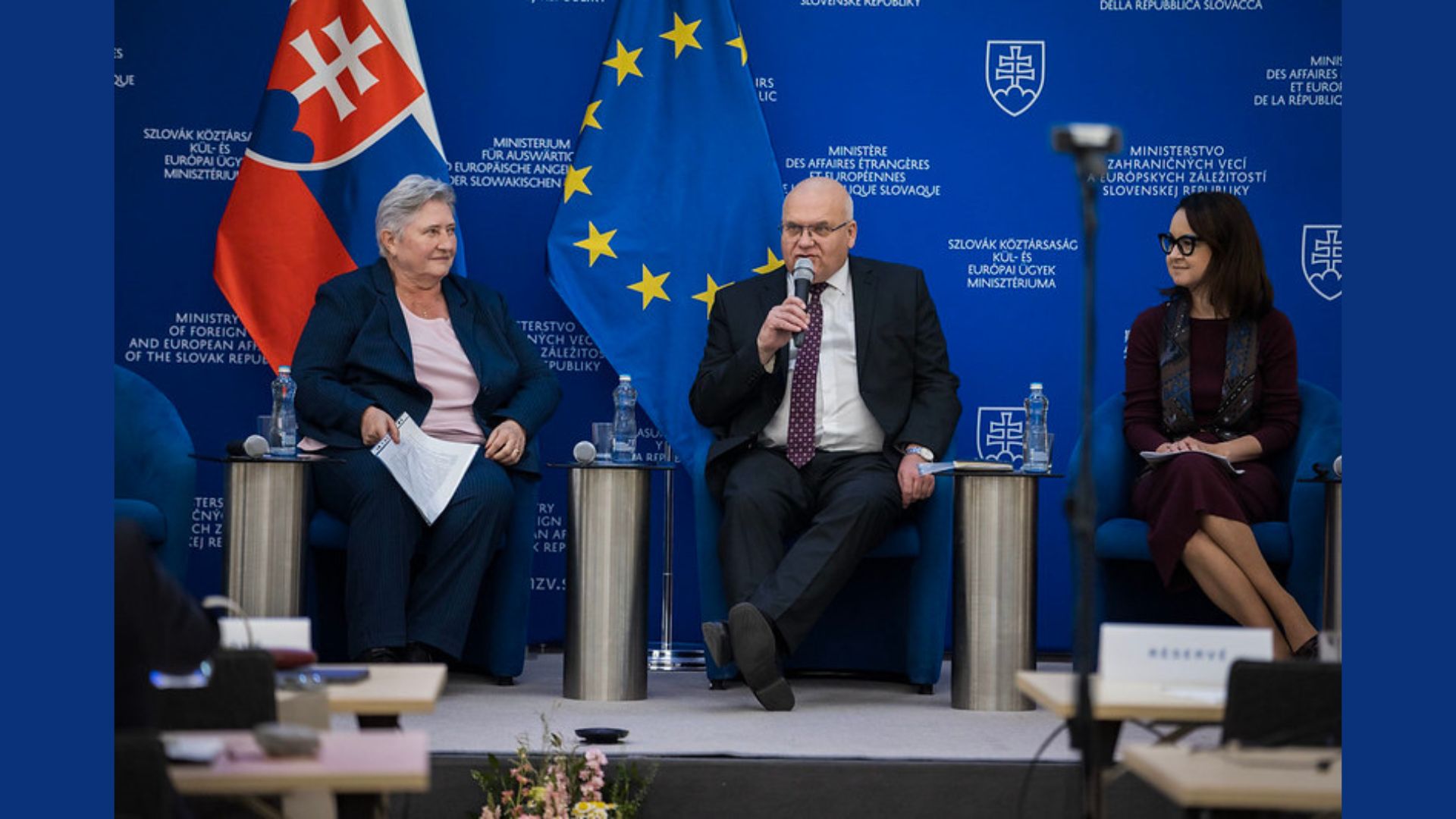 Diskutujúci na pódiu, sedia v kreslách, dve ženy, jeden muž; jedna zo žien je predsedníčka