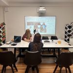 lektorky počas vzdelávania, sedia pri stole a v pozadí veľká obrazovka s online účastníkmi