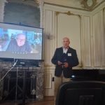 predstavenie knihy, popredseda pred publikom, na obrazovke za ním je autor knihy pripojený naživo